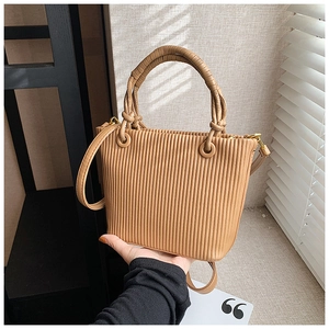 Detail showing the vertical pleated texture and khaki woven handles on the bucket bag