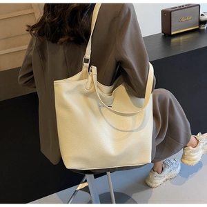 Chic cream leather tote bag shown on shoulder in a stylish lifestyle cafe setting