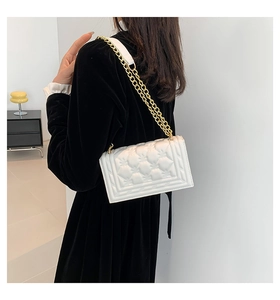 Detailed view of white quilted crossbody bag with gold chain strap on black dress