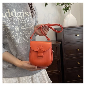Detail of bright orange crossbody bag featuring vertical stripe texture and adjustable strap