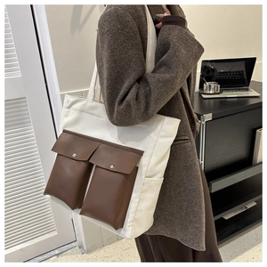 Detailed view of canvas tote bag featuring brown leather pockets and metal buckle hardware