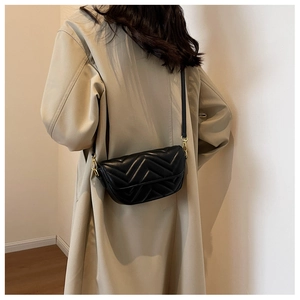 Detail of black chevron quilted crossbody bag with gold hardware worn on beige coat