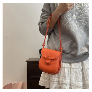 Detail of vibrant orange crossbody bag featuring vertical embossed texture and slim strap