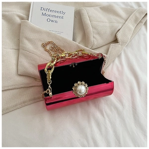 Detail of fuchsia acrylic cylinder clutch with pearl flower buckle and gold chain strap