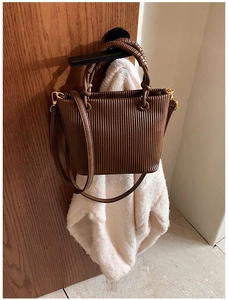 Close-up of brown pleated bucket bag with woven handle and gold hardware on door