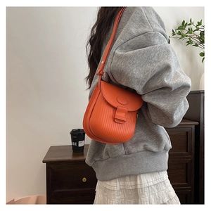 Fashionable bright orange saddle bag featuring vertical stripes and magnetic closure detail