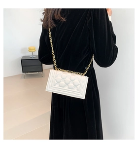 Detail of white quilted handbag featuring floral patterns and gold chain strap on a model