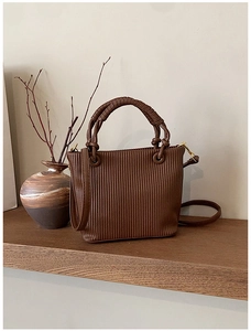 Close-up of a dark brown pleated bucket bag with spiral handle and gold hardware on wood