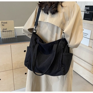 Detail view of black corduroy tote bag showing side pocket and adjustable shoulder strap