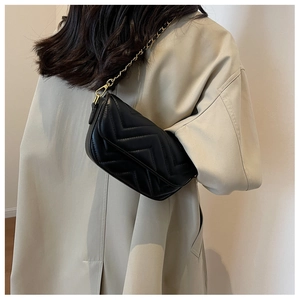 Detail of black quilted leather shoulder bag with gold chain strap worn by a model