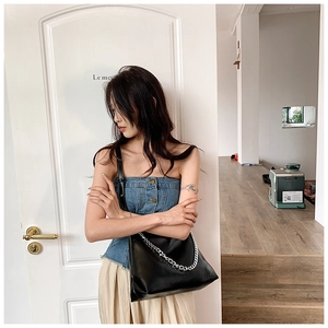 Detailed view of black leather shoulder bag with a bold silver metal chain and strap