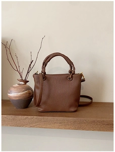 Detailed close-up of dark brown vertical pleated bucket bag on a vintage wooden shelf
