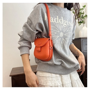 Detail of vibrant orange textured crossbody bag worn with a casual stylish outfit
