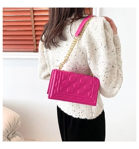 Detail of fuchsia quilted crossbody bag with gold chain strap worn by a model