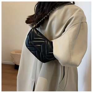Detail of black quilted shoulder bag with gold chain strap on a beige trench coat