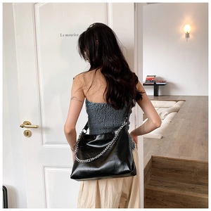 Detail of a black glossy tote bag featuring a chunky silver chain and smooth faux leather