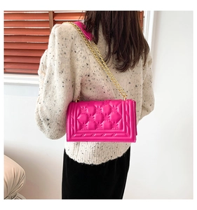 Detail of fuchsia quilted handbag with gold chain strap worn by a model in soft light