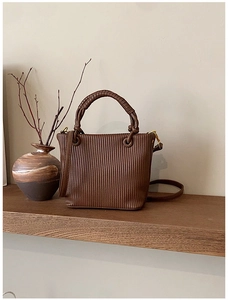 Detail of dark brown pleated bucket bag with braided handle and gold metal hooks
