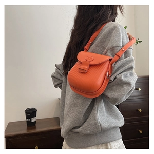 Close-up of vibrant orange crossbody bag with pleated texture and silver buckle