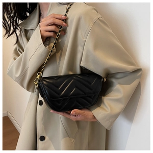 Detail of black quilted leather shoulder bag with gold chain strap on a model