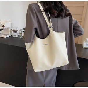Close-up of the pebbled leather texture and silver metal bar detail on ivory tote bag