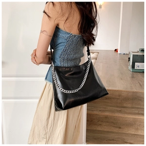 Detail of the glossy black leather tote bag with a bold silver chain handle and strap