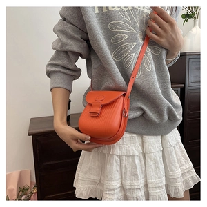 Side view of an orange leather saddle bag with textured finish and brand logo on flap