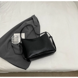 Detail of minimalist black faux leather tote bag on grey suit jacket and white sheets