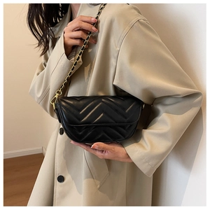 Detail of black quilted crossbody bag with V-shaped stitching and golden chain strap