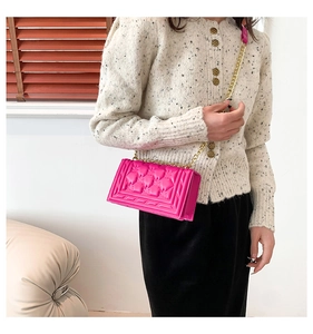 Close-up of pink quilted crossbody bag with gold chain strap worn with tweed cardigan
