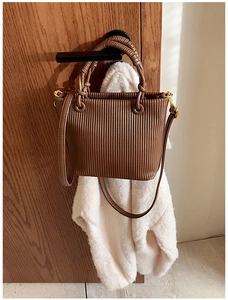 Detail of brown pleated leather bucket bag with gold hardware on a wooden door handle