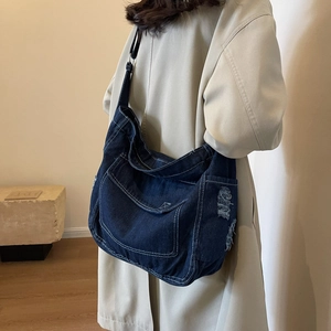 Borsa a tracolla in denim blu scuro con cuciture bianche e bordi sfrangiati su modella
