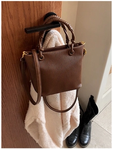 Detailed view of brown pleated bucket bag with woven handle hanging on a wooden door
