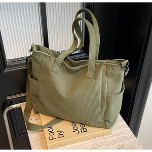 Detail of green corduroy tote bag showing side pocket, strap and matte metal buckle