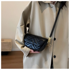 Chic black quilted crossbody bag with gold hardware worn over a beige trench coat