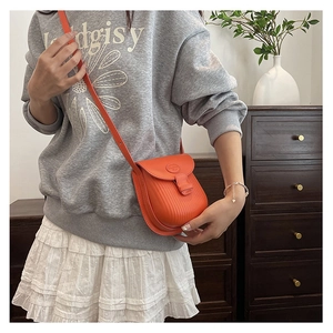 Detail of an orange pleated mini crossbody bag worn by a model in a home setting