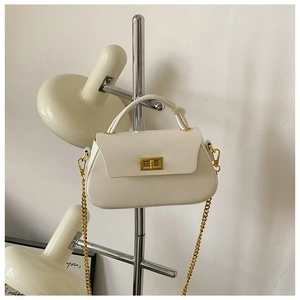 Detail view of cream-colored leather crossbody bag with golden chain and metal buckle
