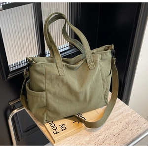Detail of olive green corduroy tote bag featuring texture and adjustable strap on stone surface