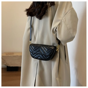 Detail of black V-quilted crossbody bag with gold hardware worn over a khaki trench coat