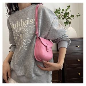 Detail view of pink crossbody bag with vertical pleats worn by a model in a home setting