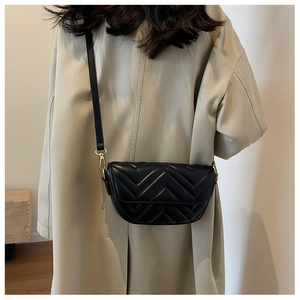 Detail of a black chevron quilted crossbody bag with gold lock on a beige trench coat