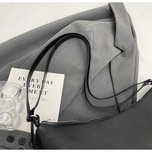 Detail of a black minimalist hobo shoulder bag with silver zipper on grey blazer background