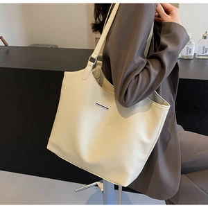 Detail showing creamy white litchi grain leather texture and metallic bar on tote bag