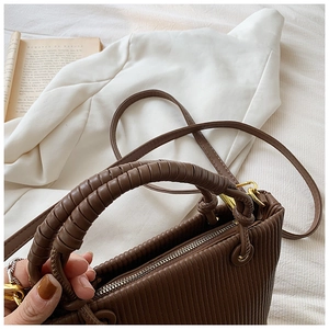 Detail of dark brown pleated bucket bag with spiral woven handle and gold zipper hardware