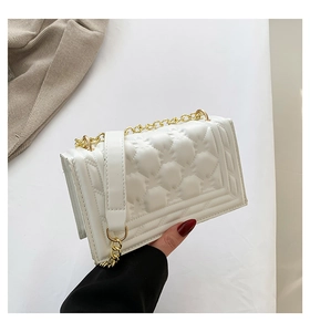 Detail of white quilted crossbody bag featuring metal chain strap and leather pad