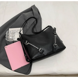 Detail of black faux leather tote bag with decorative metal zippers in a casual setting