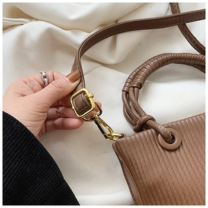 Detail showing the brown pleated leather texture and gold-tone metal buckle of the bucket bag