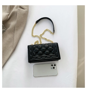 Detail view of black quilted flap bag with gold chain strap next to a smartphone