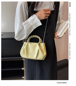 Detail of light yellow pleated handbag featuring woven handle and silver chain strap