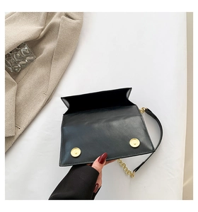 Detail of black leather handbag featuring dual magnetic buckles and gold metal chain strap
